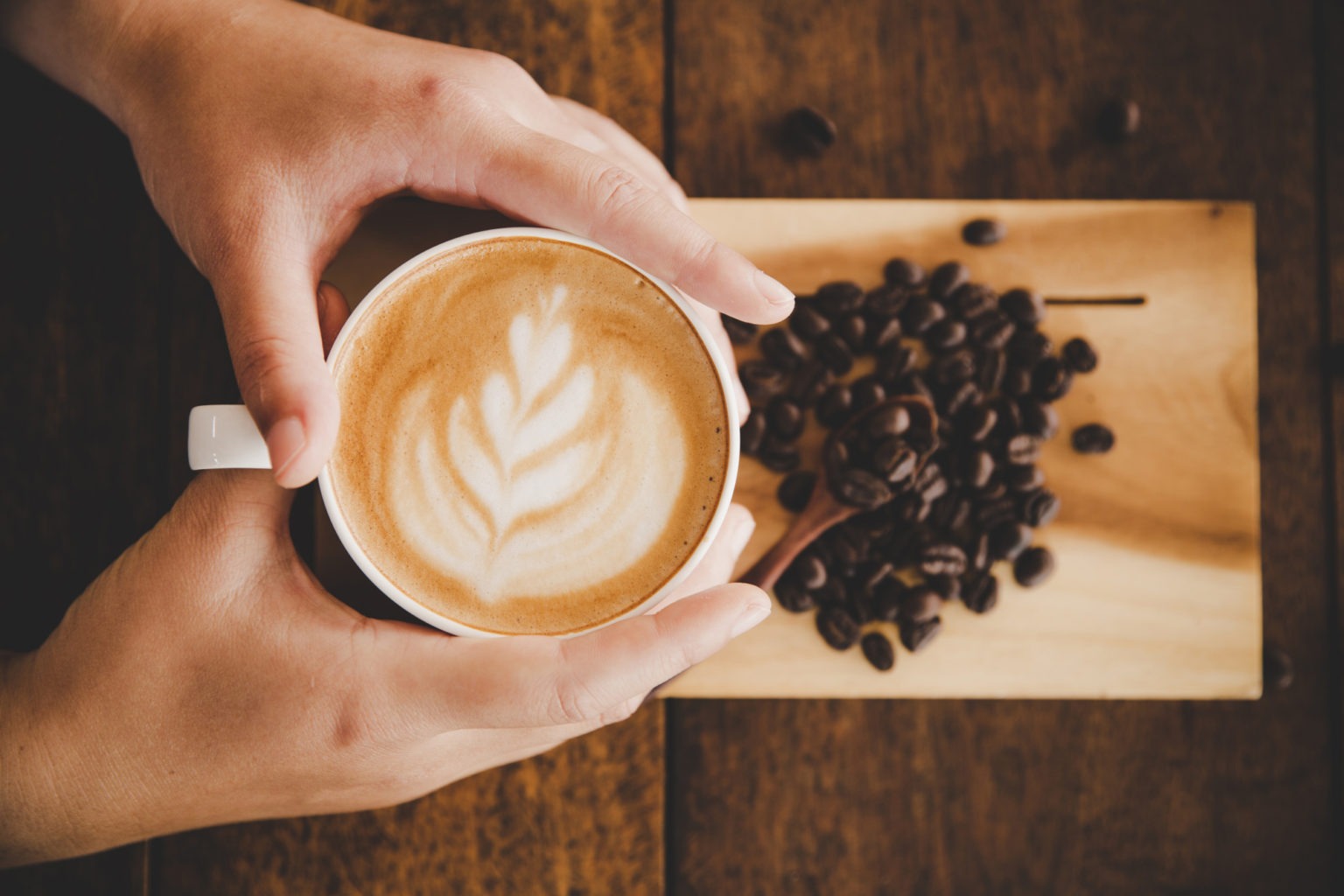 mano sosteniendo taza de cafe con granos de café al fondo